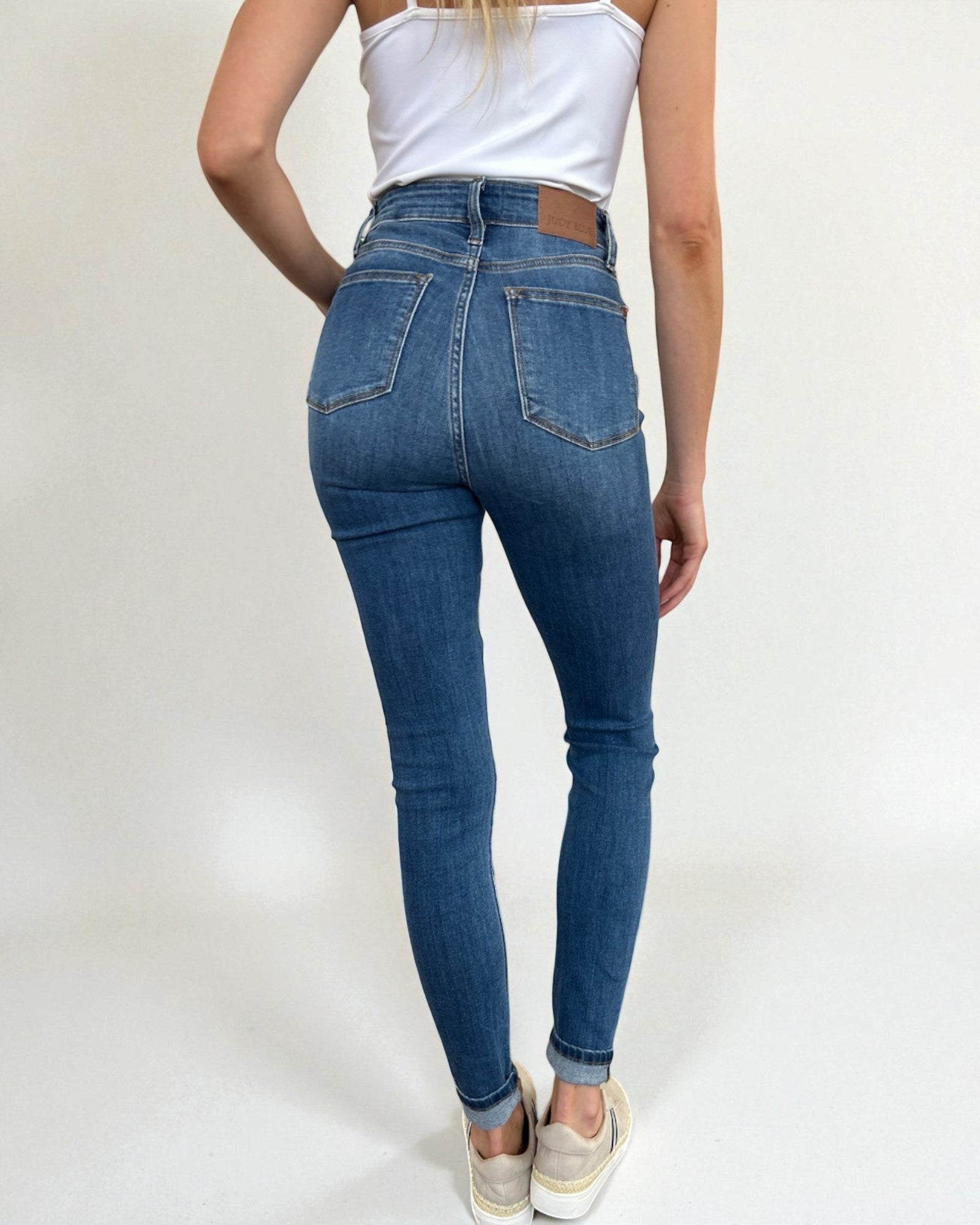 Person wearing blue jeans and a white top on a plain background