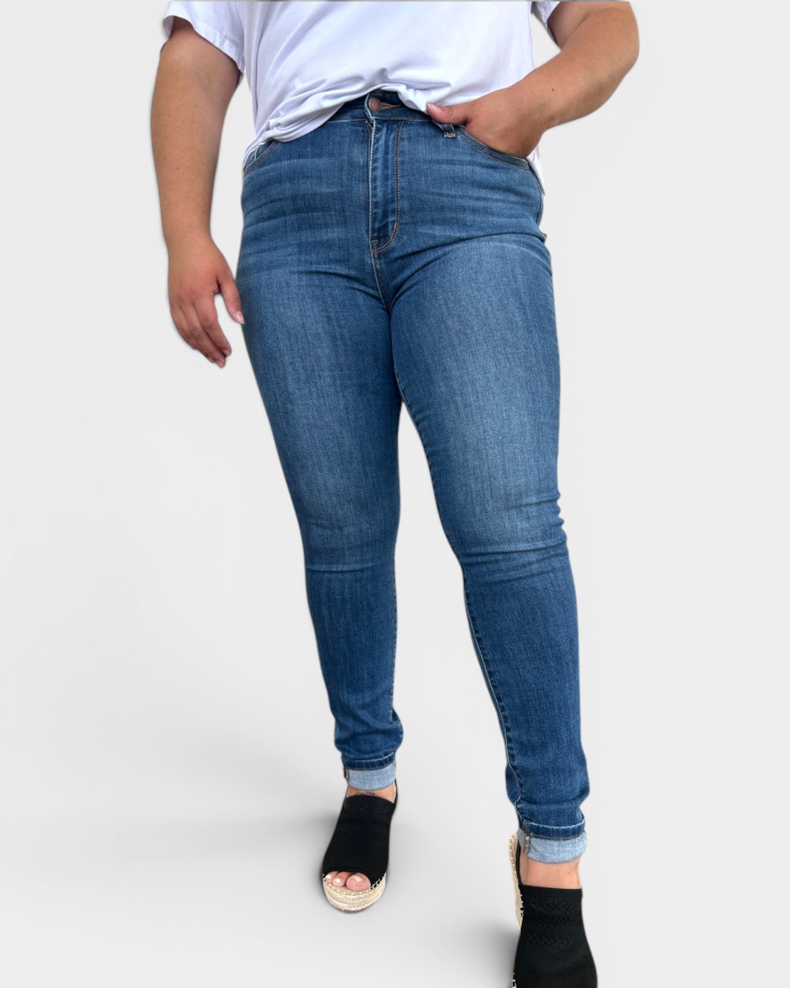 Person wearing blue jeans and a white top on a plain background