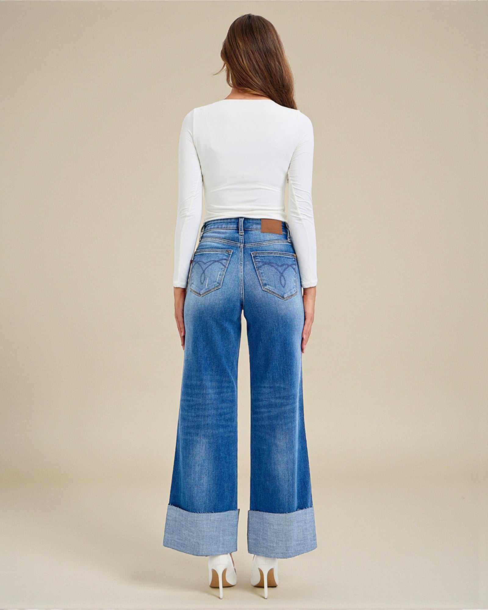 Woman wearing blue wide-leg jeans and a white long-sleeve top on a beige background