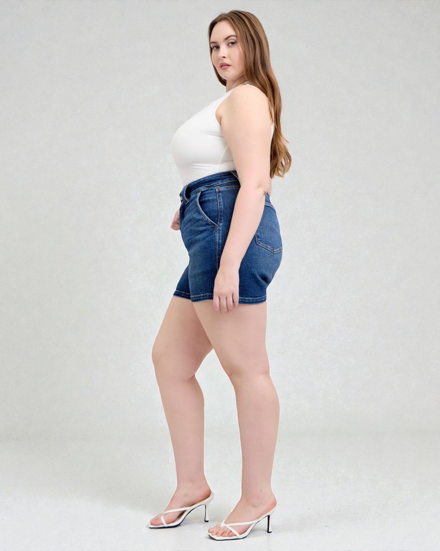 Woman wearing a white top and blue denim shorts on a plain background