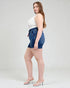 Woman wearing a white top and blue denim shorts on a plain background