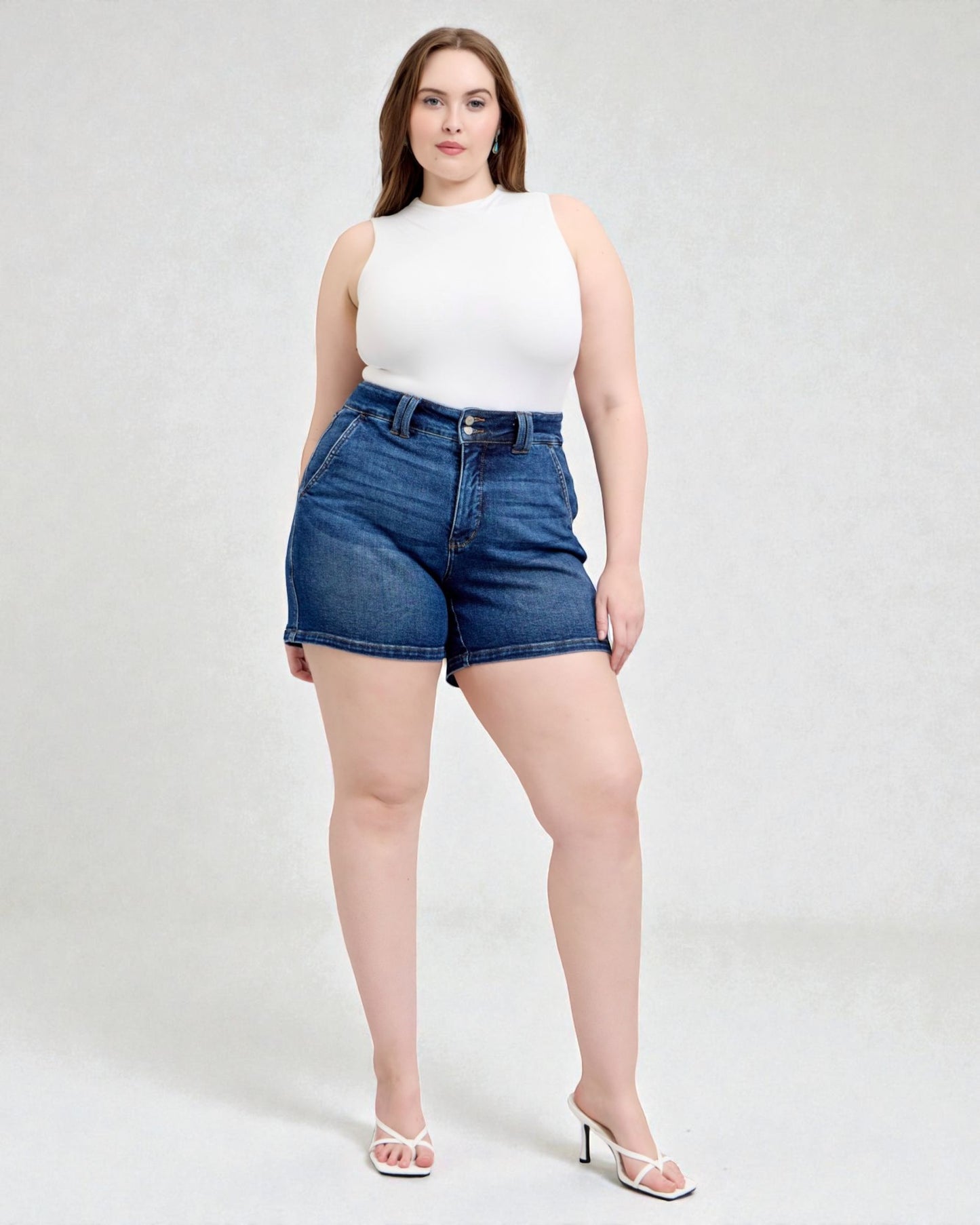 Woman wearing a white sleeveless top and blue denim shorts on a white background