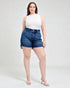 Woman wearing a white sleeveless top and blue denim shorts on a white background