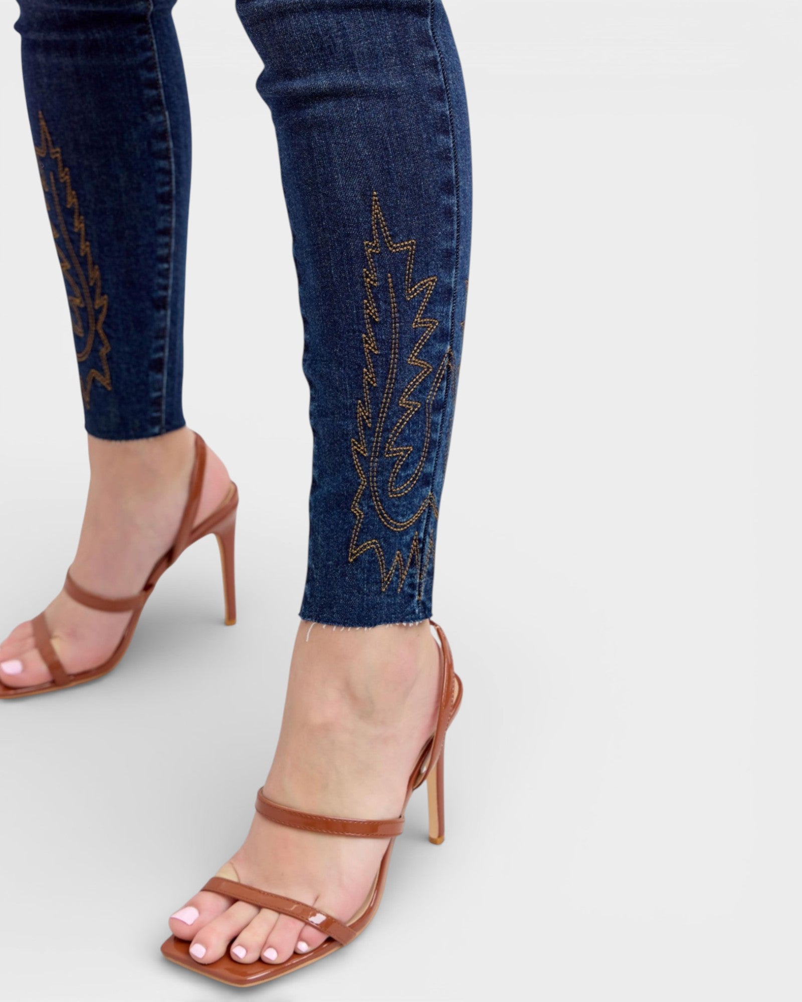 Person wearing blue jeans with embroidery and brown sandals on a light gray background