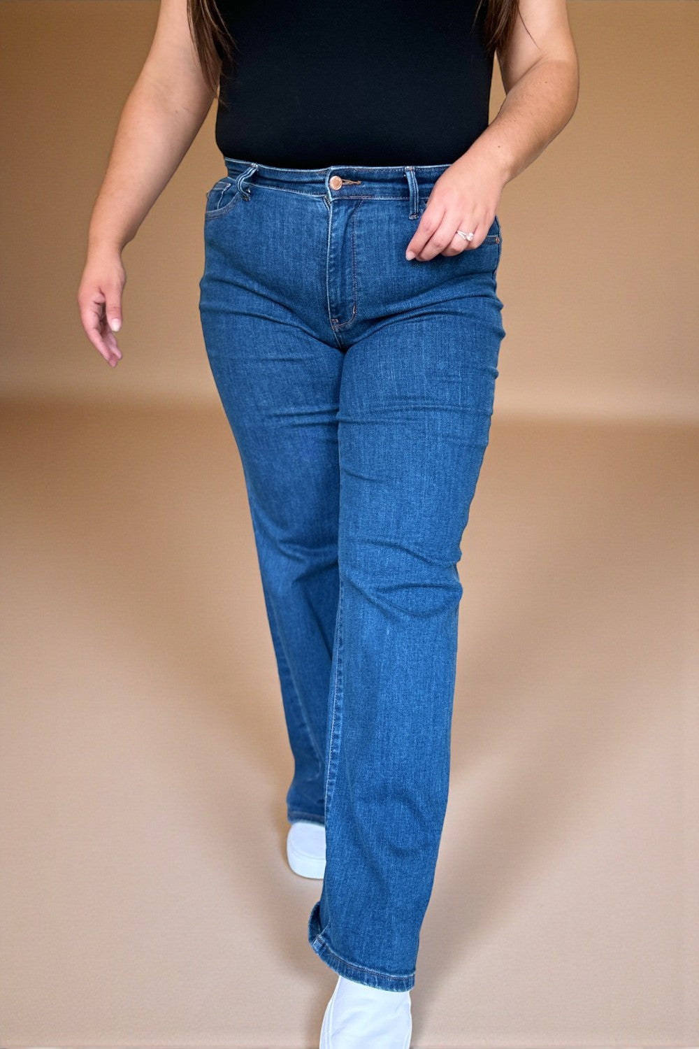 Person wearing blue jeans and a black top on a beige background