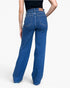 Rear view of a person wearing blue wide-leg jeans with a black top, shown against a light gray studio background.