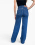 Rear view of a model wearing blue wide-leg jeans with a black top, shown against a plain white studio background.