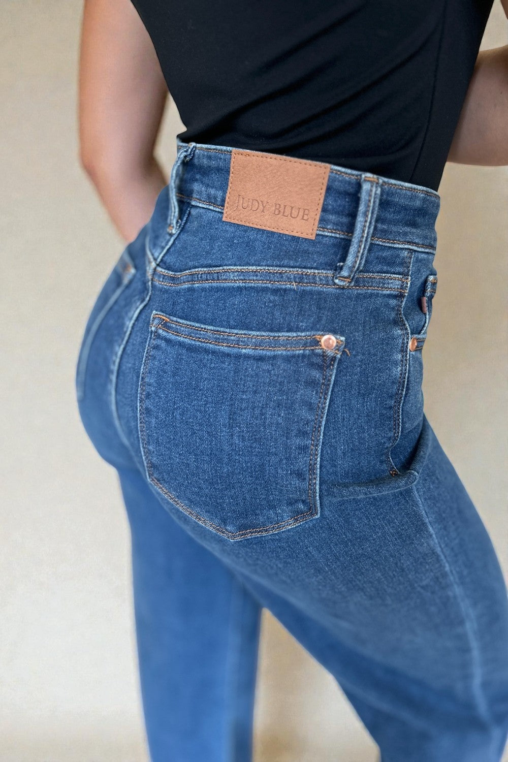 Person wearing blue jeans with a visible brand label on a plain background