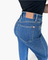 Close-up back view of a person wearing blue denim jeans with a black top, showing the waistband, belt loops, back pocket, and a tan leather patch that reads JUDY BLUE.
