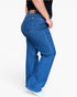 A person wearing blue wide-leg jeans, shown from the back and side against a plain light gray studio background.