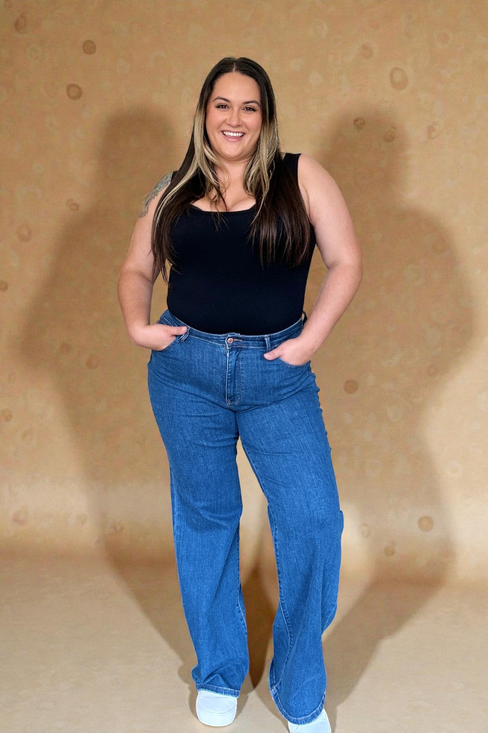 Woman wearing a black top and blue jeans against a beige background