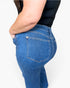 Close-up side and back view of a person wearing blue denim jeans with a black top against a light gray studio background.