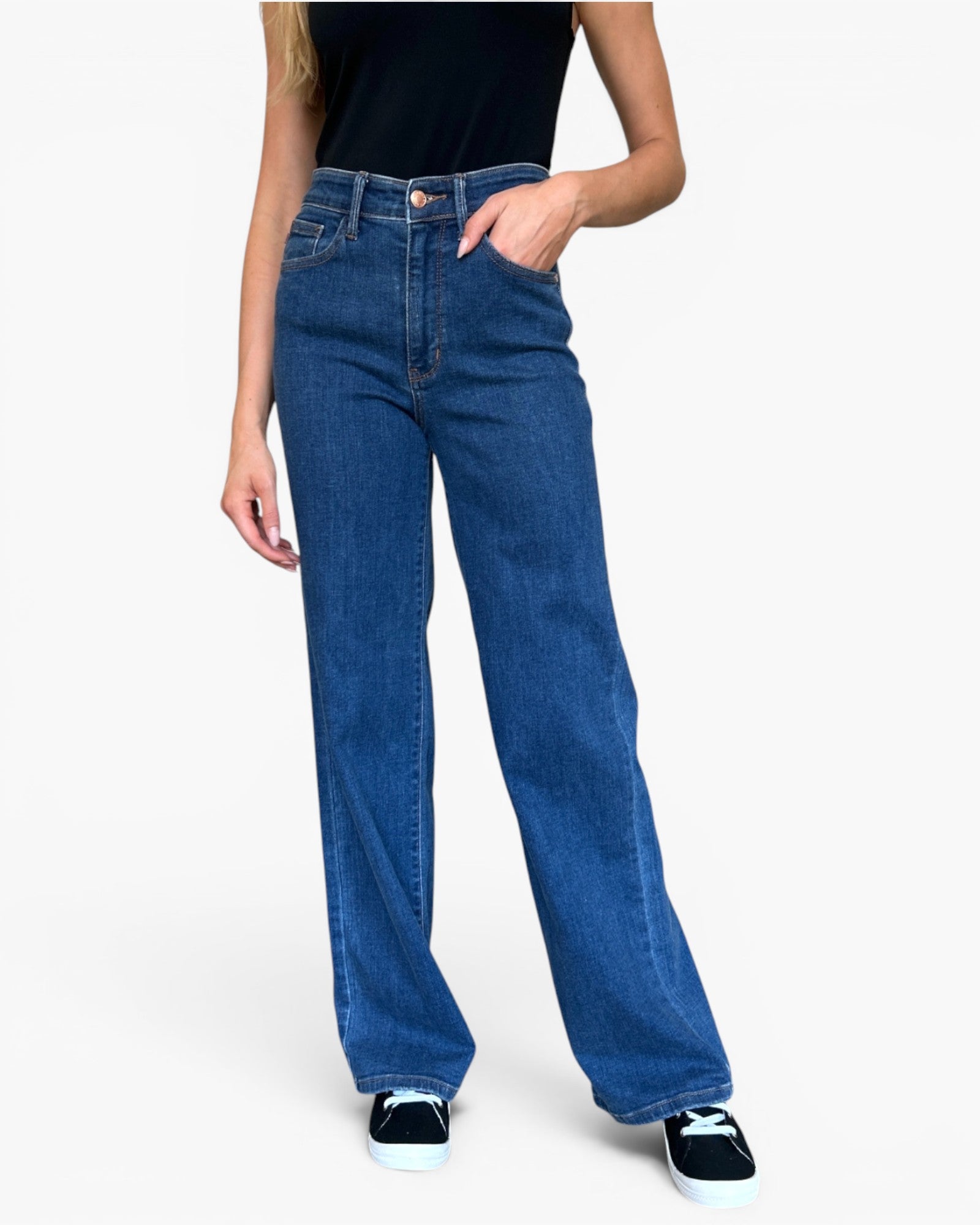 A model wearing a pair of high-waisted, wide-leg blue denim jeans with a black top and black sneakers, shown from the waist down on a light gray background.
