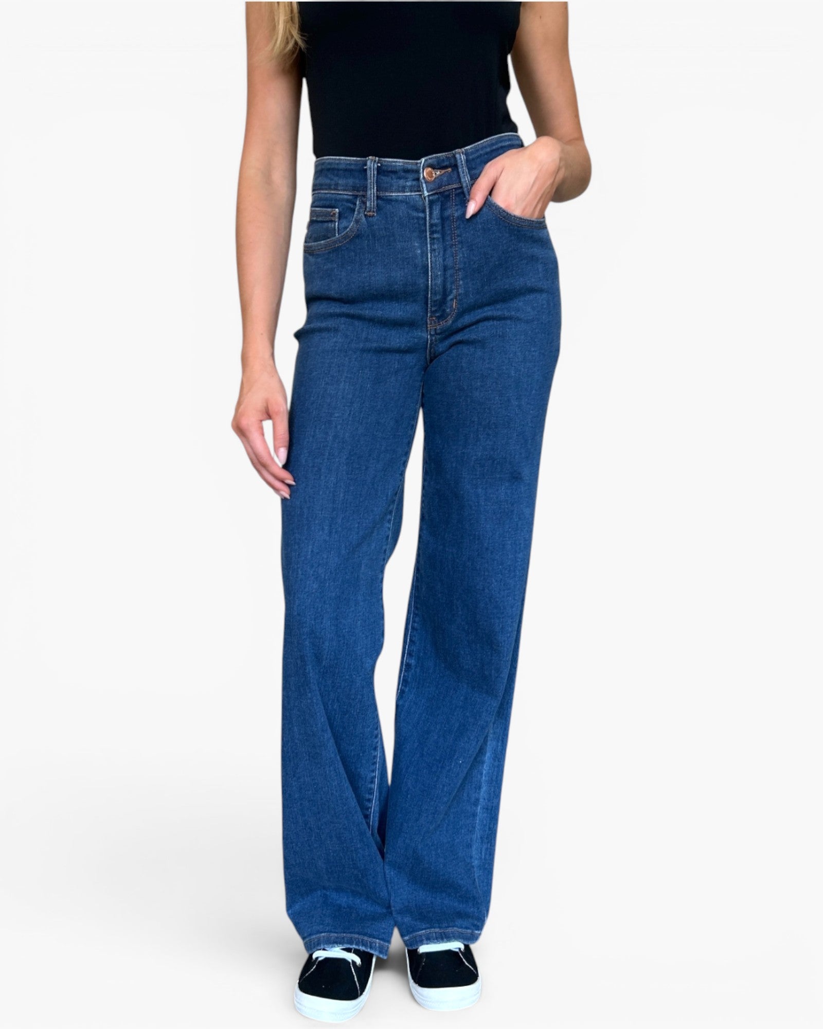 A model wearing a pair of high-waisted, wide-leg blue denim jeans with a black top and black sneakers, shown from the waist down on a light gray background.