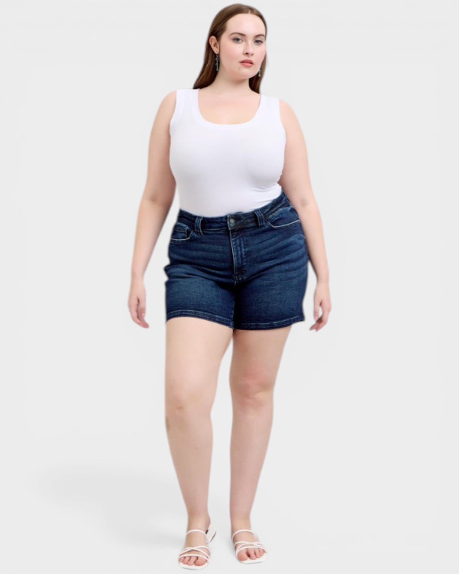 Woman wearing a white tank top and blue denim shorts on a white background