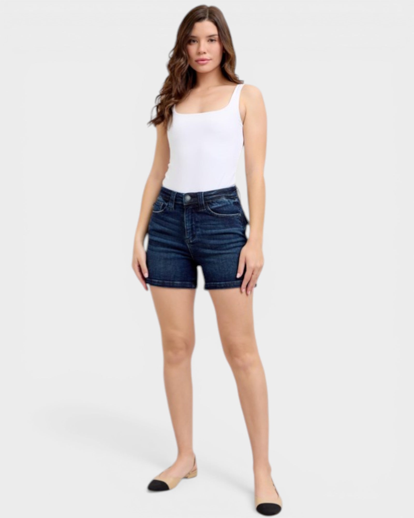 Woman wearing a white tank top and blue denim shorts on a white background