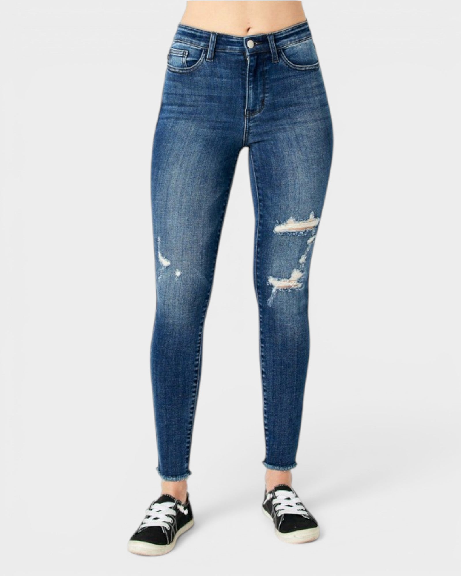 A person wearing blue skinny jeans with distressed rips on the thighs and knees, paired with black low-top sneakers, shown against a light gray studio background.