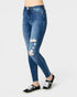 A person wearing blue skinny jeans with distressed rips on the thighs and knees, paired with black low-top sneakers, shown against a light gray studio background.