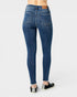 Rear view of a person wearing blue skinny jeans and black slip-on shoes against a light gray studio background.