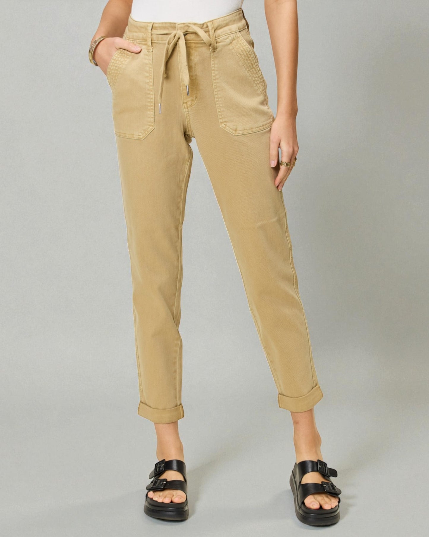 Person wearing beige pants with a tie waist on a gray background