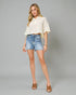 Woman wearing a white lace top and denim shorts on a gray background