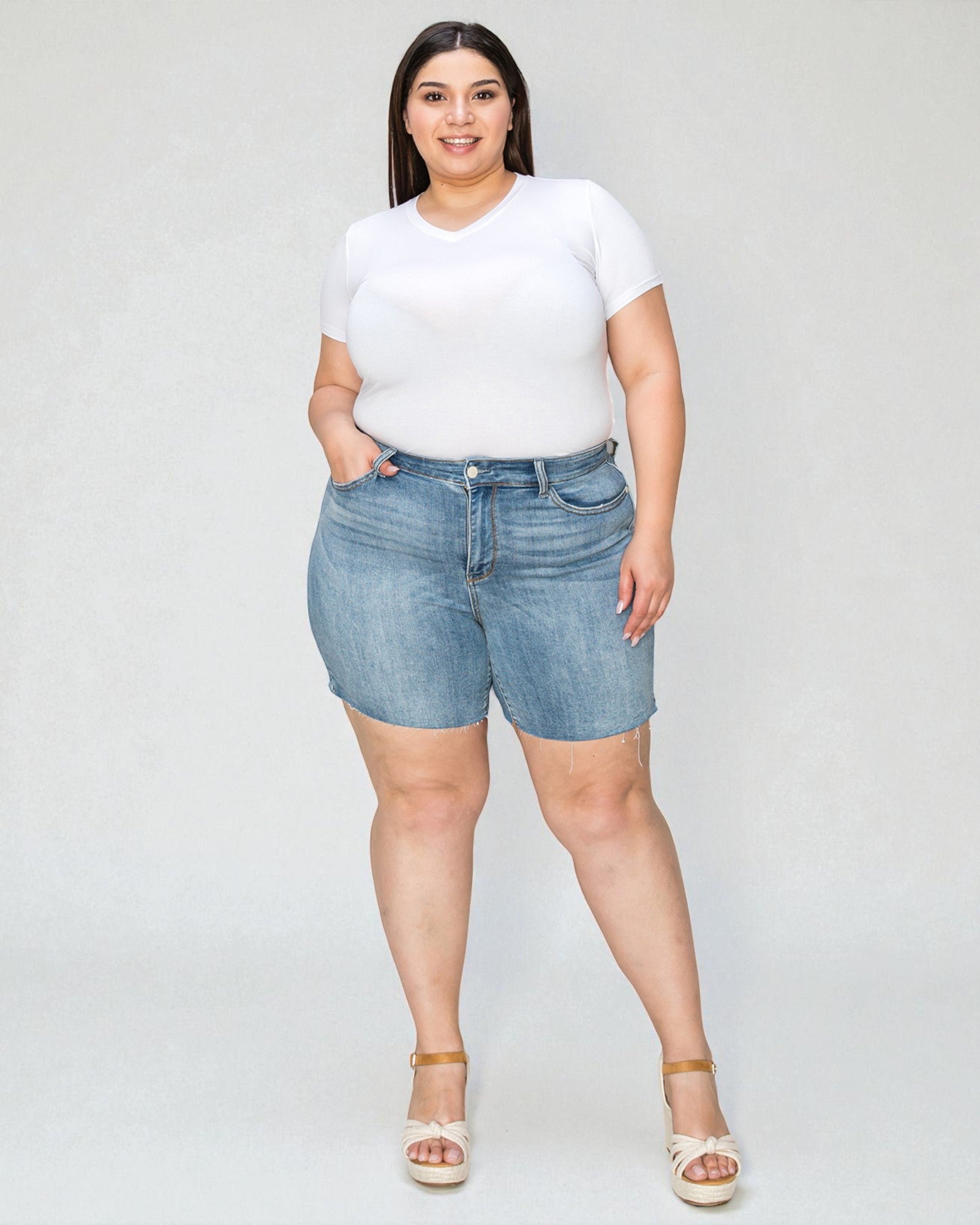Woman wearing a white t-shirt and denim shorts on a plain background