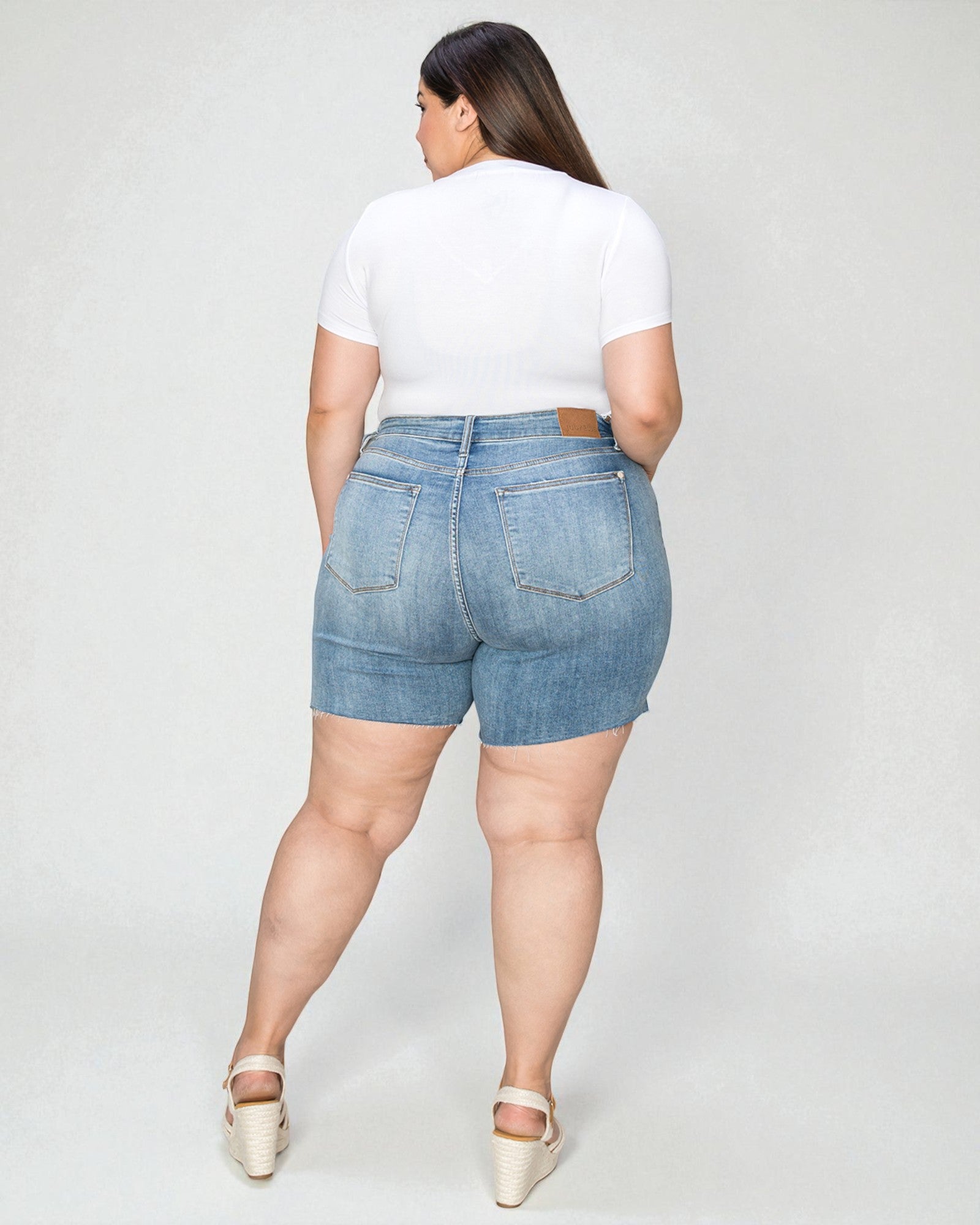 Person wearing denim shorts and a white top on a plain background