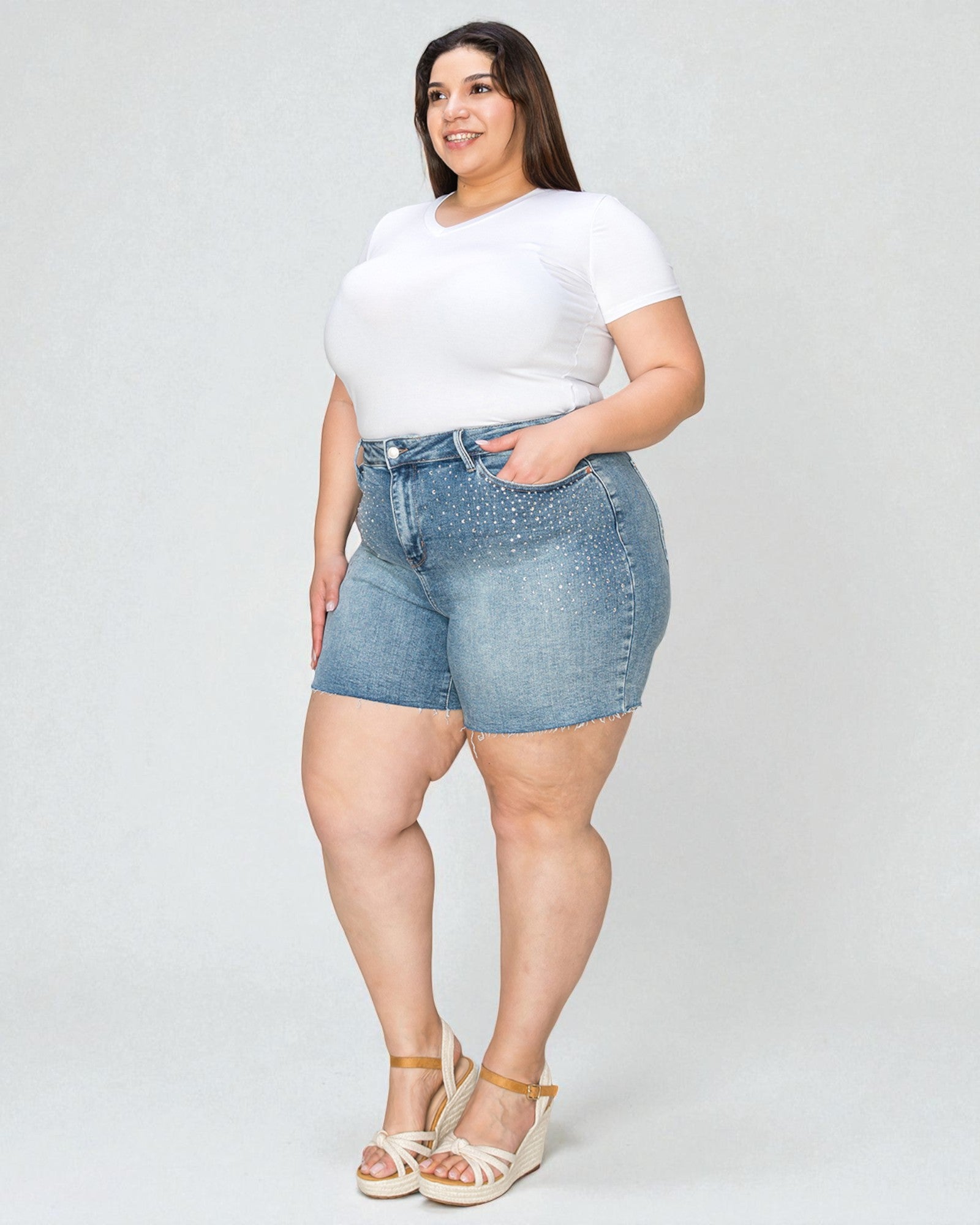 Woman wearing a white t-shirt and denim shorts on a plain background