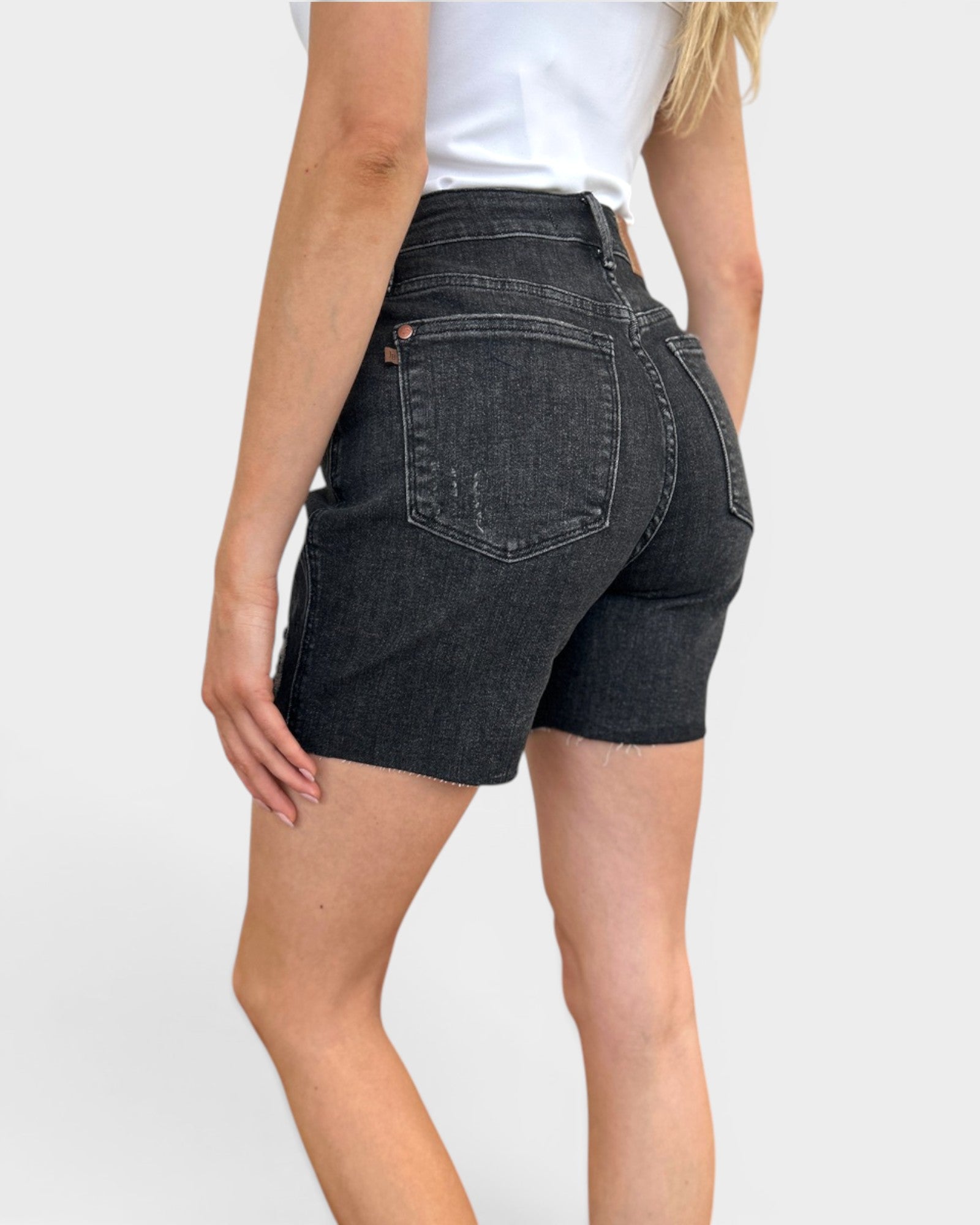 Person wearing black denim shorts on a white background