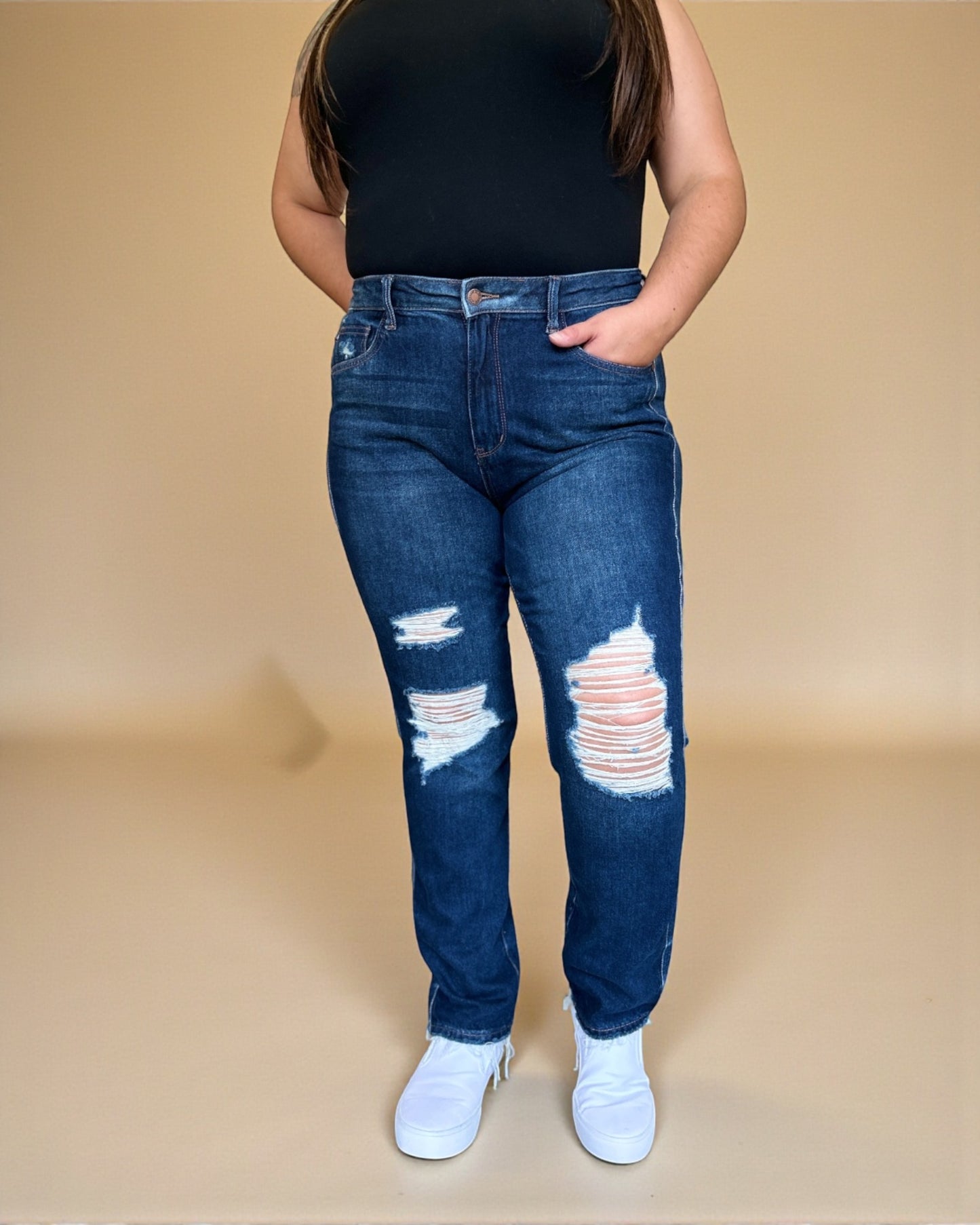 Person wearing blue distressed jeans and a black top on a beige background