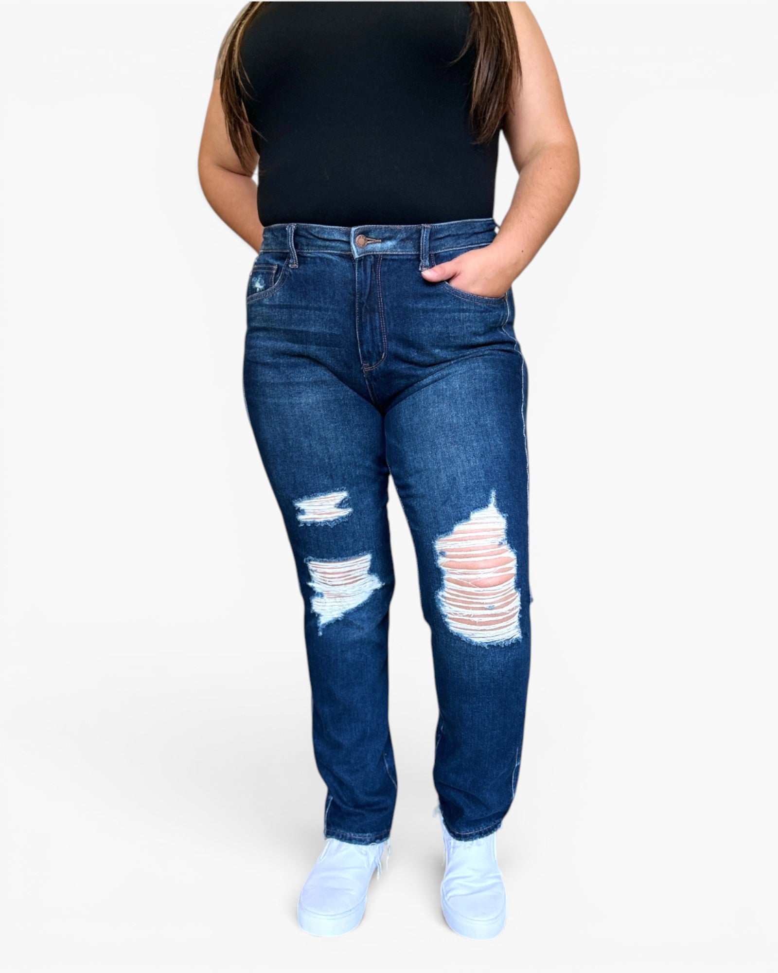 A person wearing dark blue distressed denim jeans with ripped details on the thighs and knees, paired with a black sleeveless top and white sneakers, shown against a plain light gray background.