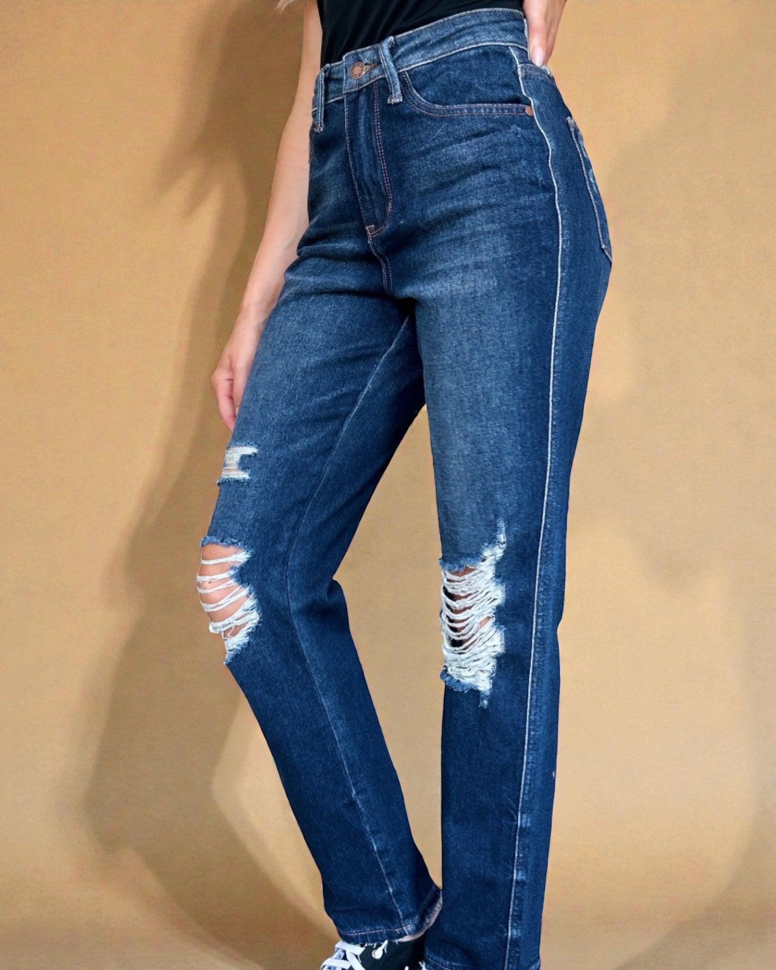 Person wearing blue jeans with distressing details on a beige background