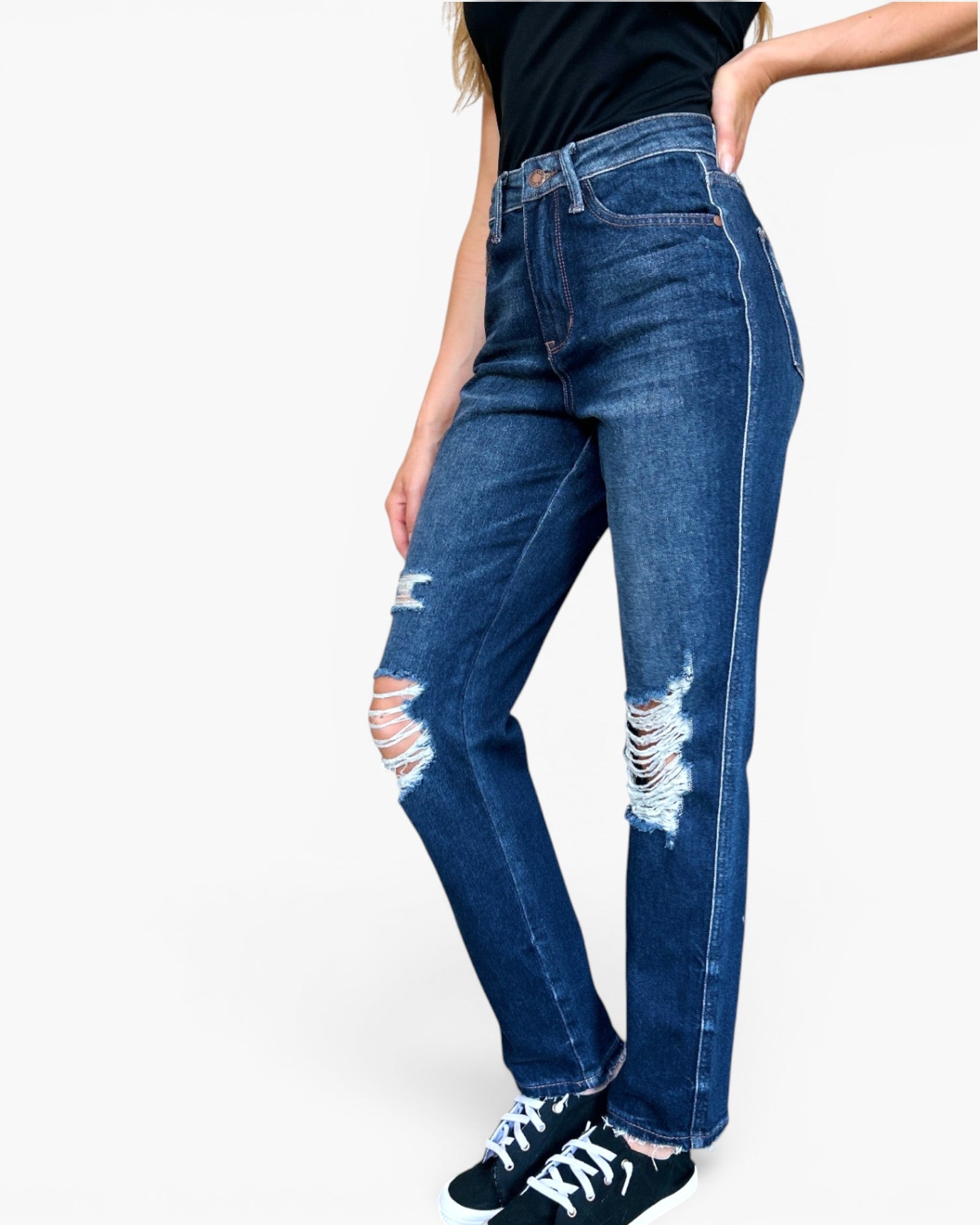 A person wearing dark blue high-waisted distressed jeans with ripped details on the thighs, paired with a black top and black sneakers, shown against a plain white background.