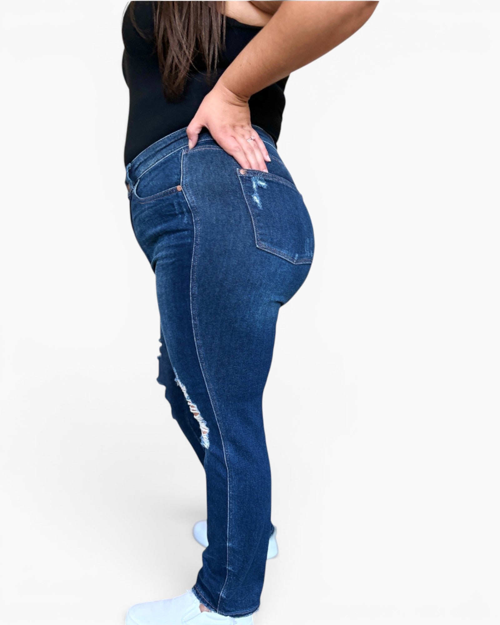 A person wearing dark blue distressed skinny jeans, shown from the side and back against a plain white studio background.