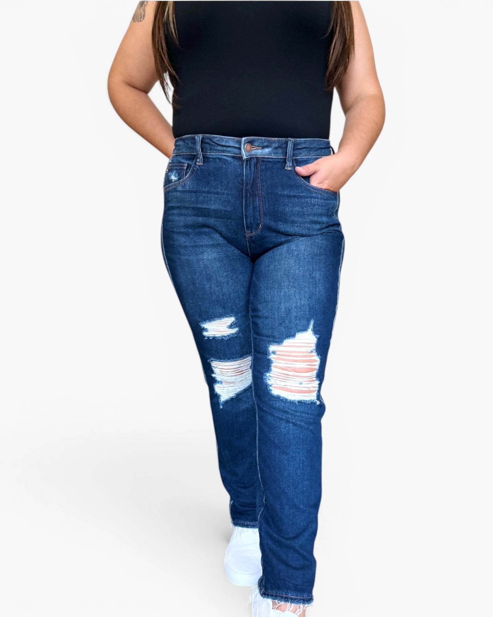 A person wearing high-waisted blue denim jeans with distressed rips at the knees, paired with a black sleeveless top and white sneakers, shown against a plain light gray background.
