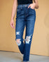Person wearing distressed blue jeans against a beige background