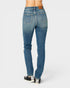 Rear view of a person wearing medium-wash blue denim jeans with black and white sneakers, shown against a light gray studio background.