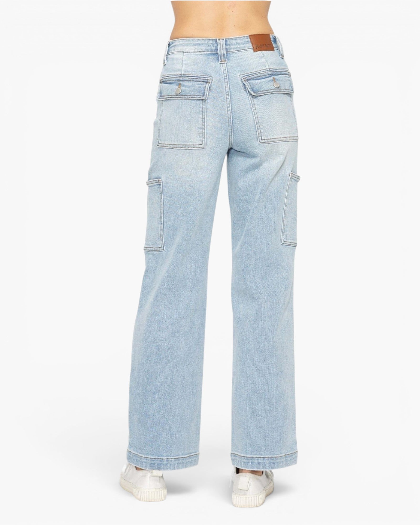 Light wash blue denim cargo pants shown from the back on a model, featuring a brown leather patch on the waistband and utility cargo pockets on the legs, paired with white sneakers against a plain white background.