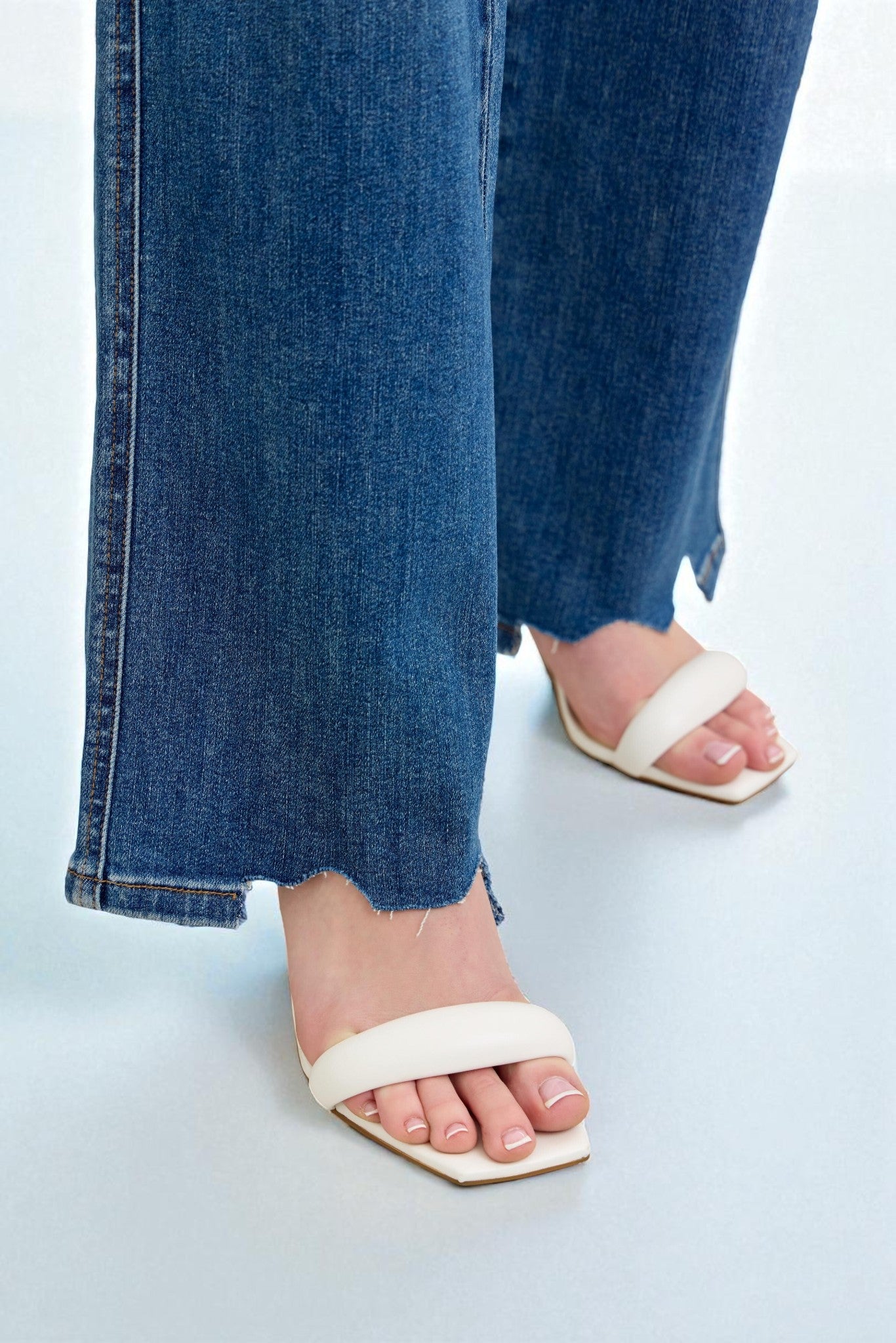 Close-up of a person wearing blue jeans and white sandals on a light blue background