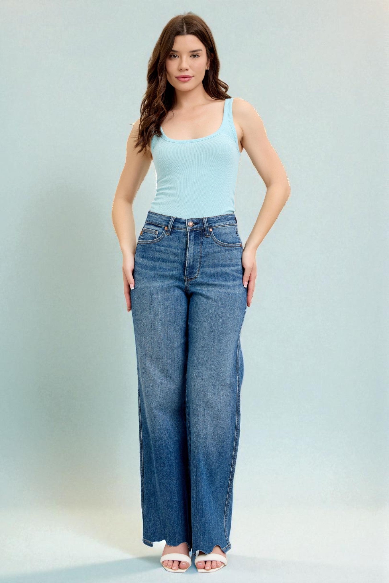 Woman wearing a light blue tank top and blue jeans against a light gray background