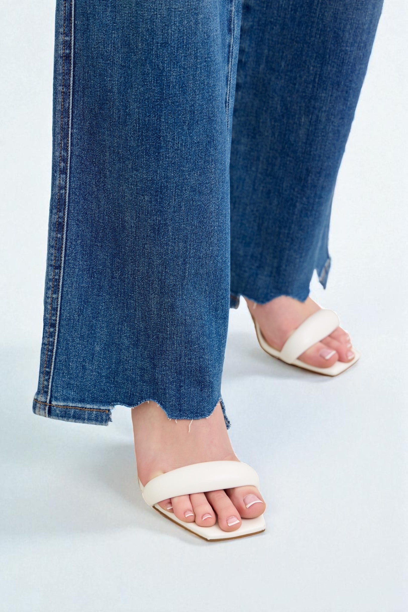 Close-up of blue jeans and white sandals on a light background