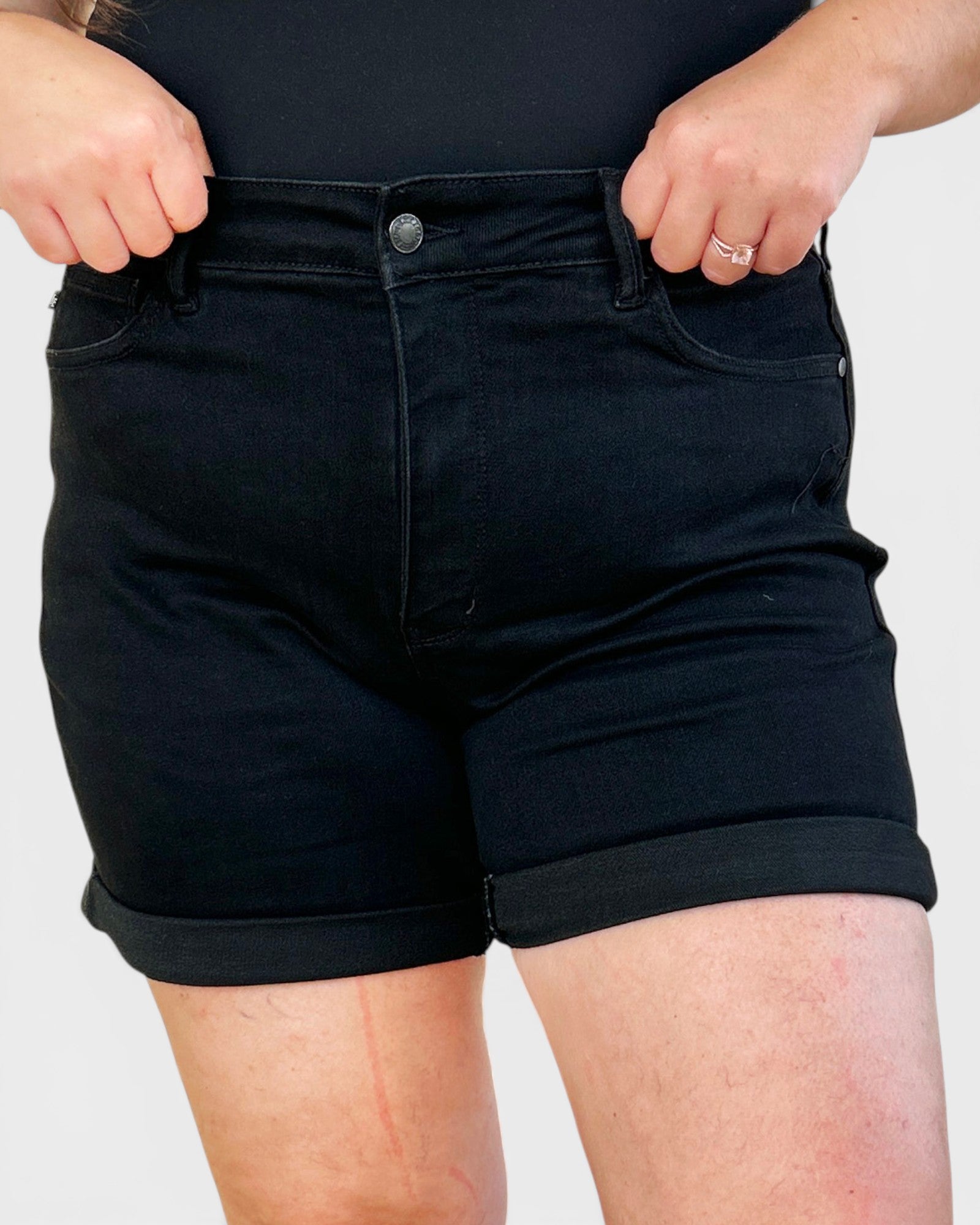 Person wearing black denim shorts on a plain background