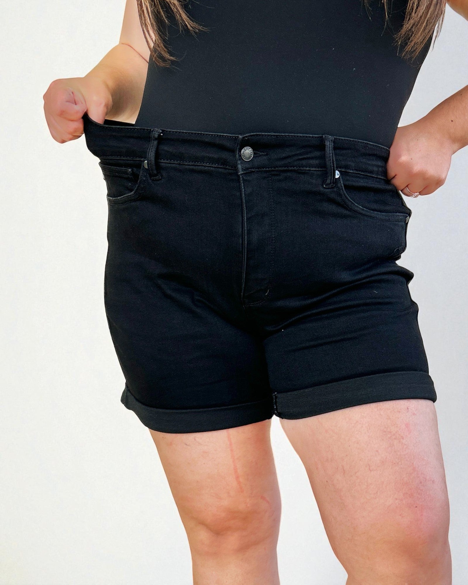 Person wearing black denim shorts on a plain background