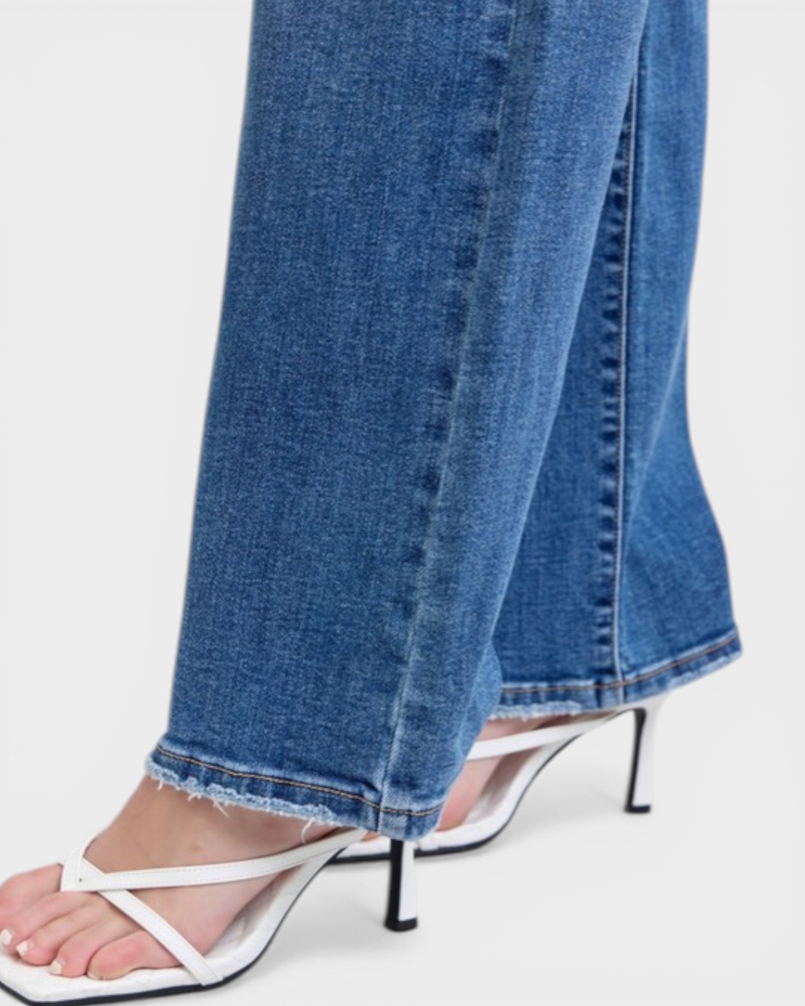 Close-up of blue jeans with white sandals on a white background
