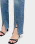 Close-up of blue jeans with a slit and black sandals on a white background