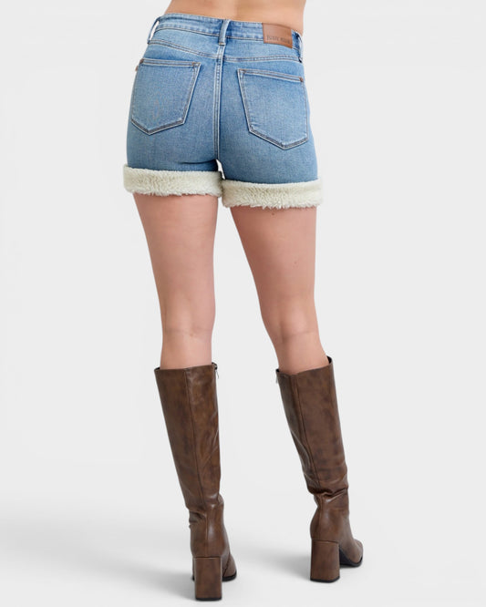 Person wearing denim shorts with white trim and brown knee-high boots on a white background