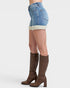 Person wearing denim shorts with white trim and brown knee-high boots on a light gray background