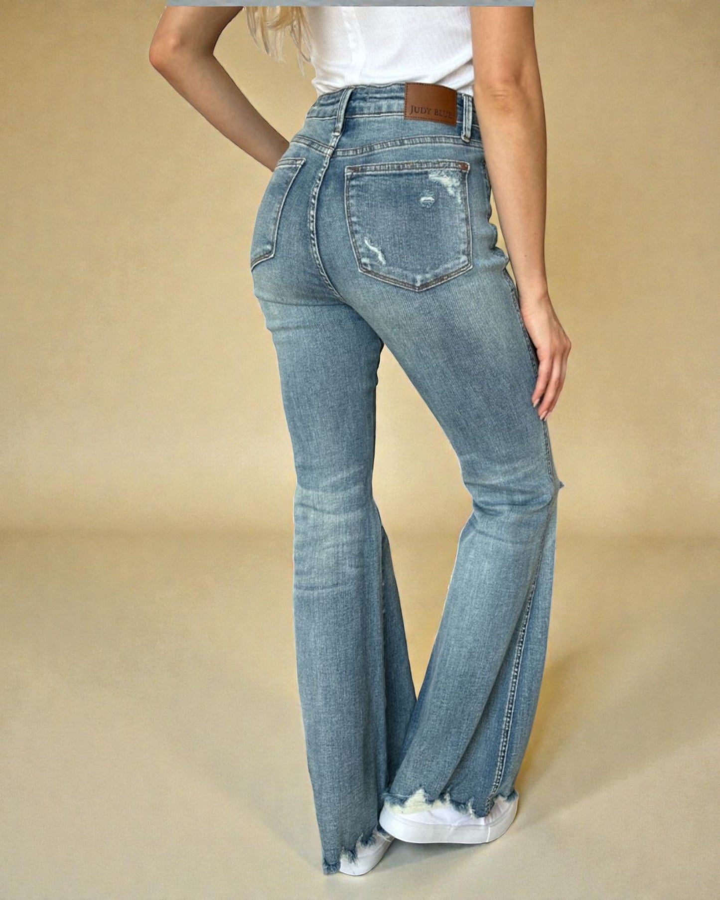 Person wearing light blue flared jeans on a beige background
