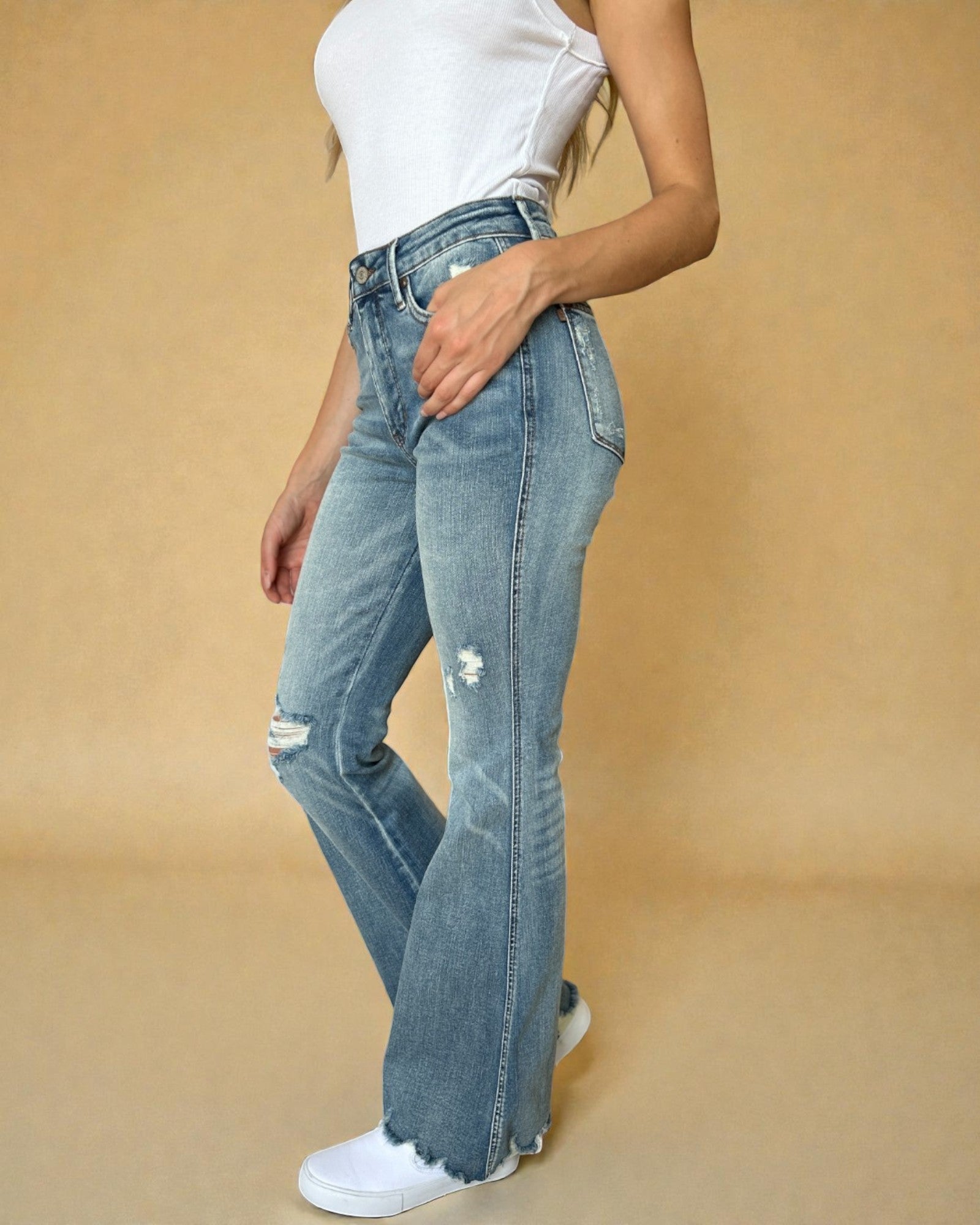 Person wearing light blue flared jeans and white sneakers on a beige background