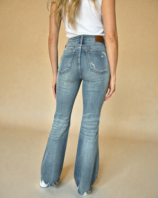 Person wearing blue flared jeans and a white top on a beige background